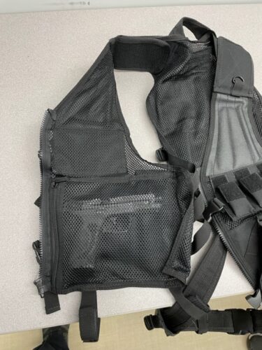 A tactical vest with mesh fabric pockets. A handgun can be seen inside.