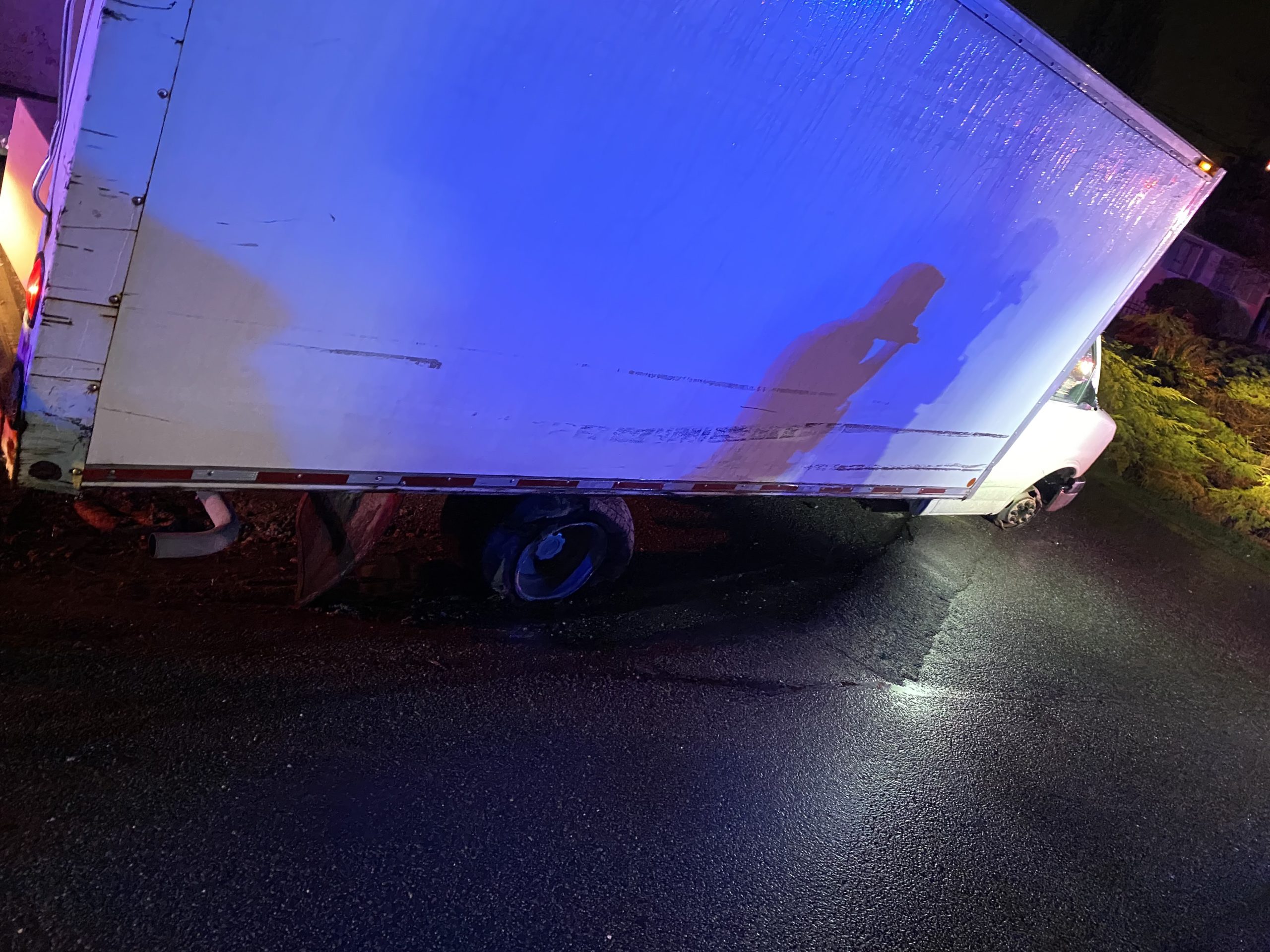 A white cube van with flat tires is illuminated by blue and red police lights