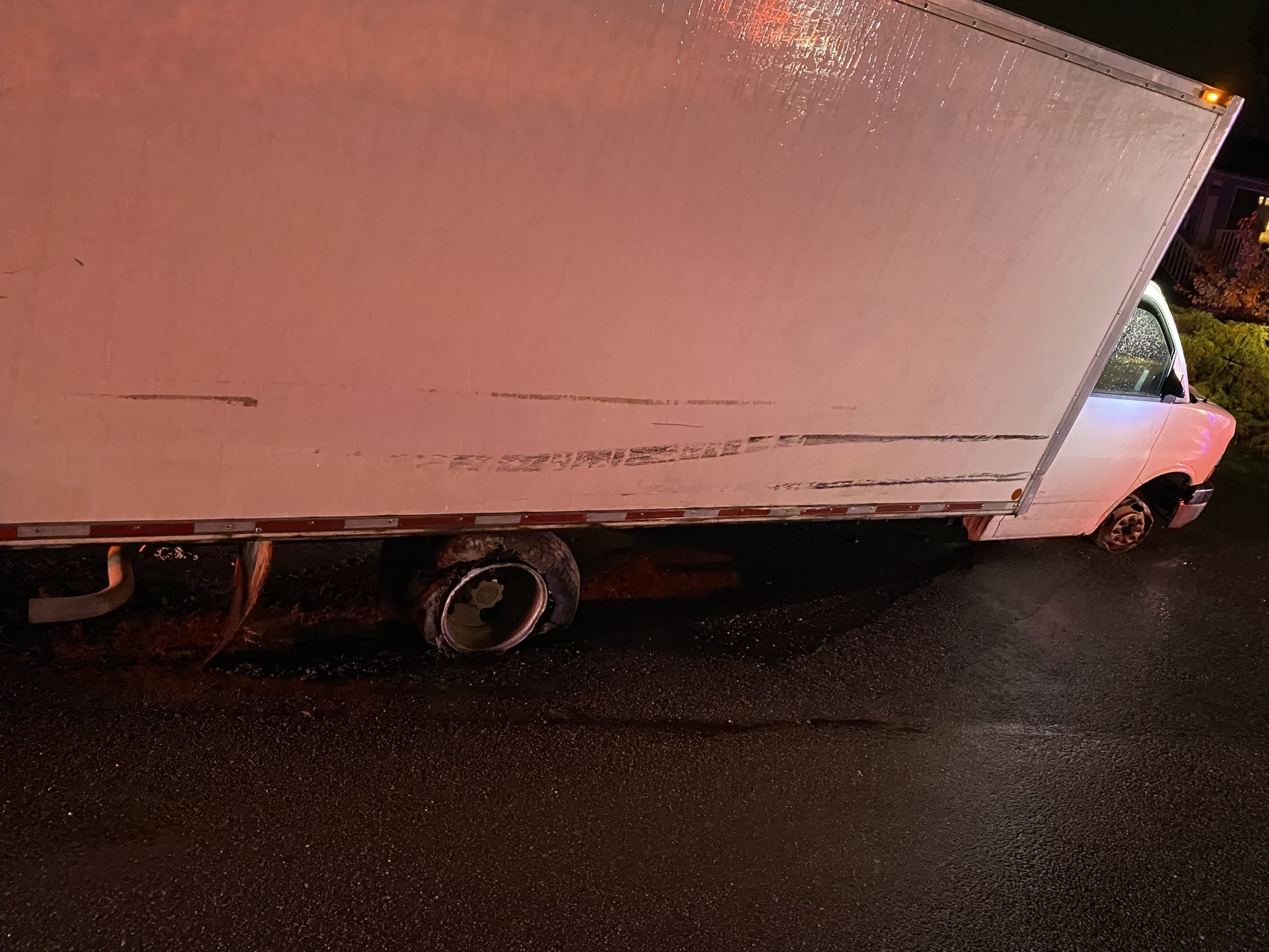 A white cube van with flat tires is illuminated by blue and red police lights