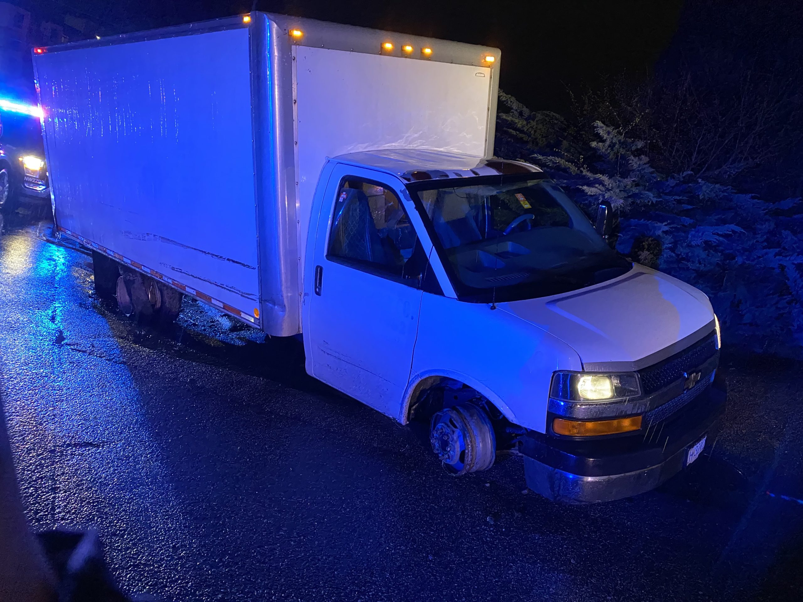 A white cube van with flat tires is illuminated by blue and red police lights