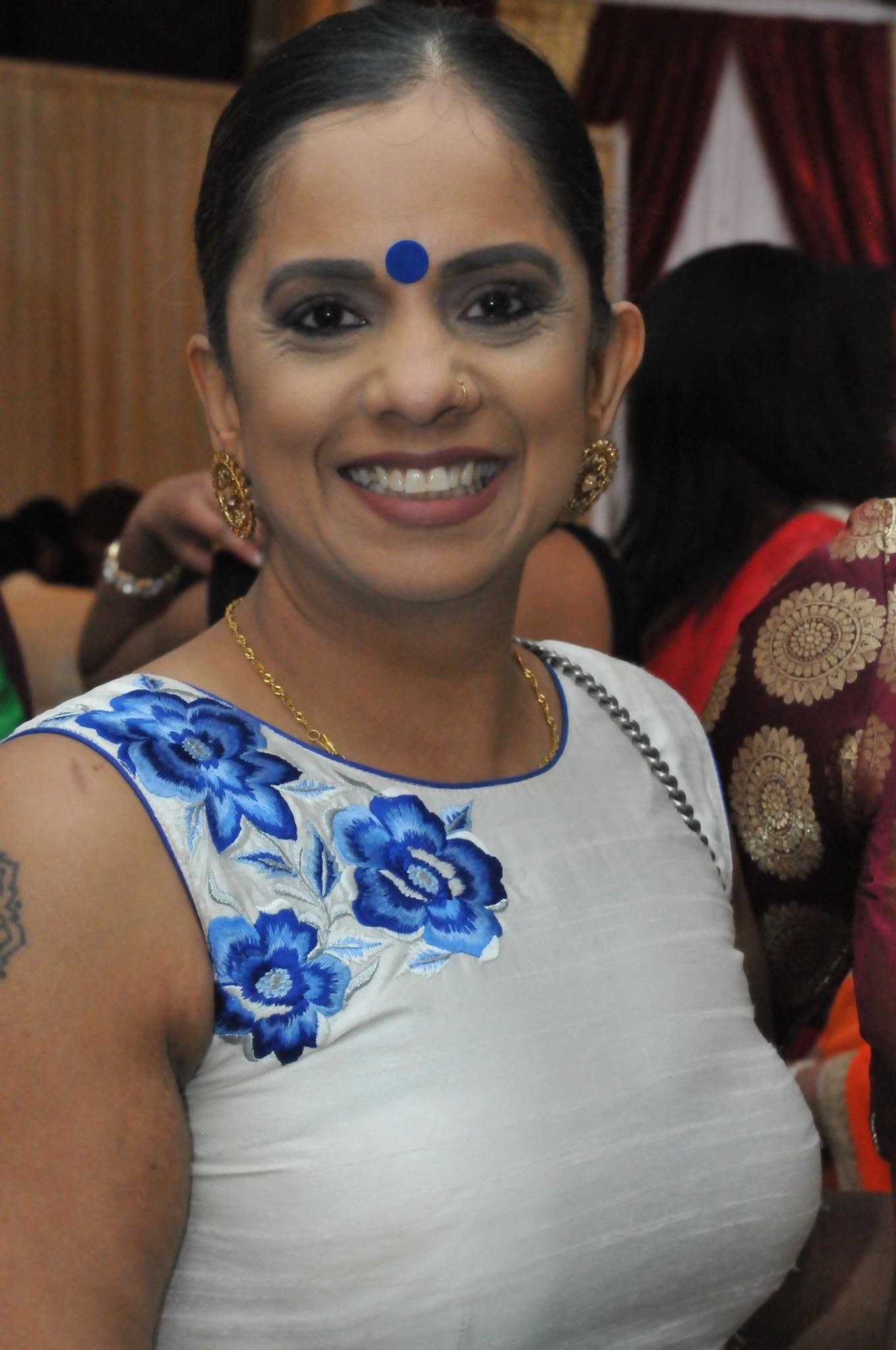 Missing person Nirla Sharma is shown smiling wearing a blue dress and gold jewlery. She has brown eyes, brown hair, and a medium complexion.