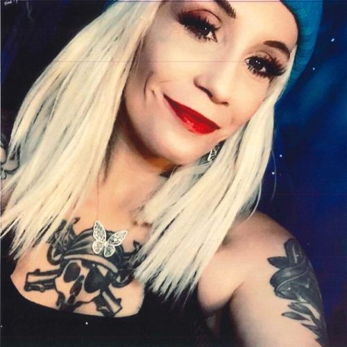 Laura Nazarek has on a blue hat, red lipstick, and tattoos on her shoulders and chest.