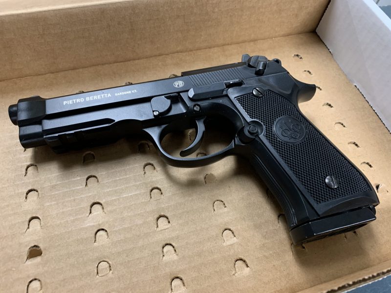 A black replica handgun is in a cardboard evidence box.