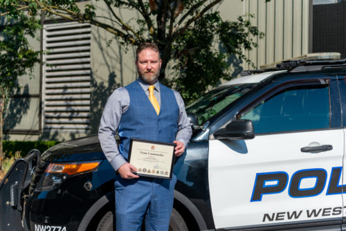 Sergeant Robson hold his Team Commander accreditation and stands in front of an NWPD patrol car.